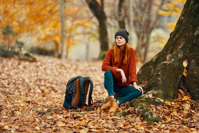 Full length of young woman sitting on tree during autumn