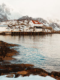 Scenic view of lake by houses against snowcapped mountains during winter