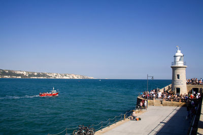 People on lighthouse by sea against clear sky