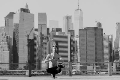 Full length of shirtless mature man practicing yoga on building terrace against one world trade center