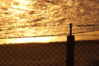 Close-up of chainlink fence against sky during sunset