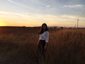 Young woman standing on grassy field against sky during sunset
