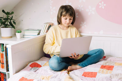 Distance learning online at home. a schoolgirl girl is sitting on a bed with a laptop in her room. 
