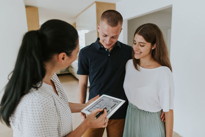 Woman with digital tablet talking with couple standing on floor at home