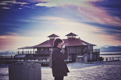 Portrait of young woman standing at beach against sky
