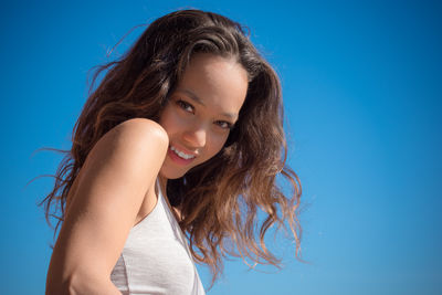 Close-up portrait of smiling young woman against blue background