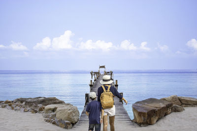 Rear view of mother with son walking on pier over sea against sky