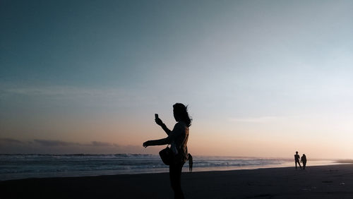 Woman at beach against sky during sunset