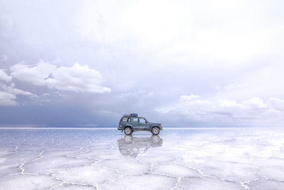 Side view of car on frozen lake against sky