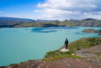 Rear view of man standing on rock against sky