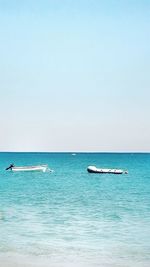 Boats in sea against clear blue sky