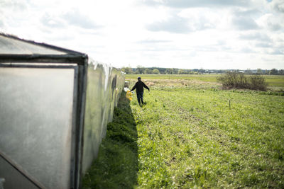 Rear view of man walking by retaining wall on grassy field against sky