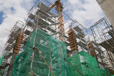 Low angle view of crane by building against sky