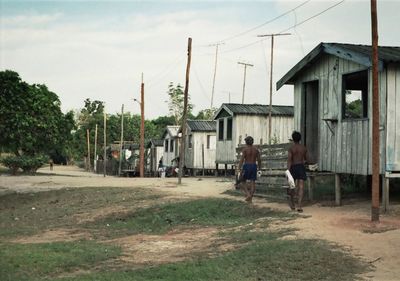 Rear view of boys walking on road by huts