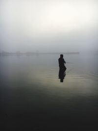 Silhouette man in lake against sky