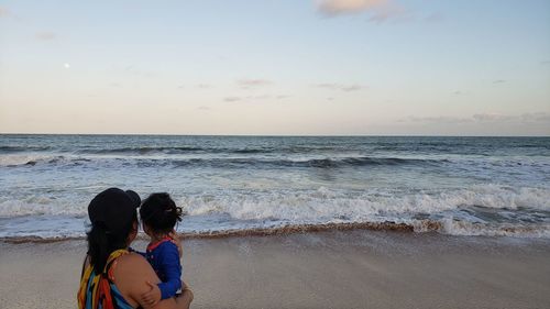 Rear view of women with daughter standing at beach against sky