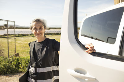 Portrait of smiling senior female engineer standing next to van at power station