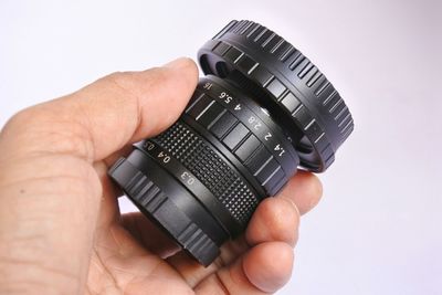 Close-up of hand holding camera lens against white background