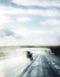 Car moving on wet road against cloudy sky