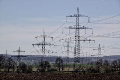 Low angle view of electricity pylons on field against sky