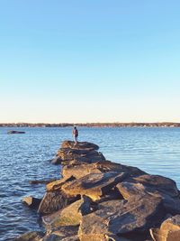 People standing on rock by sea against clear sky
