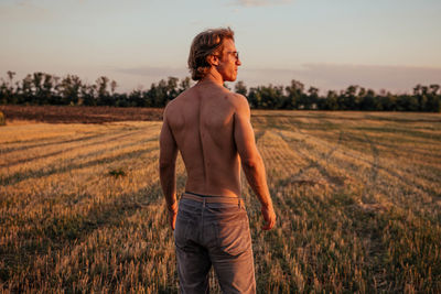 Rear view of shirtless man standing on field against sky
