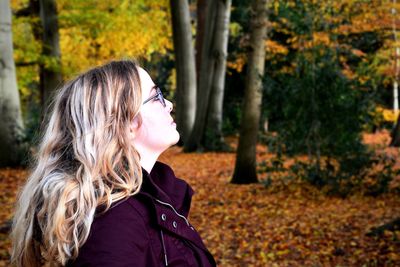 Side view of young woman standing in forest during autumn