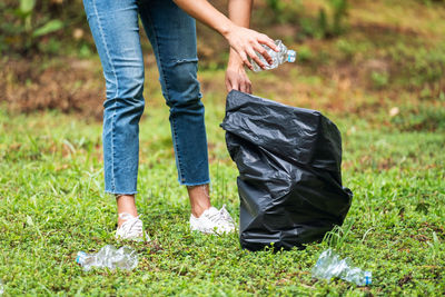 A female picking up garbage plastic bottles into a plastic bag in the park for recycling concept