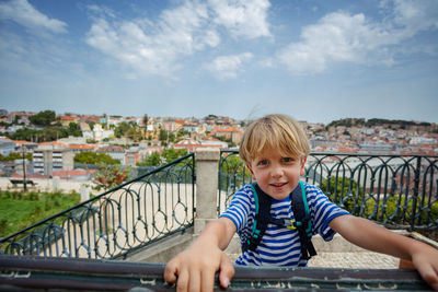 Portrait of smiling girl sitting on railing against sky