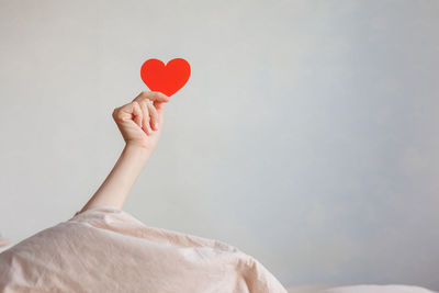 Cropped hand holding heart shape against wall