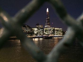 Illuminated shard building seen through chainlink fence in city at night