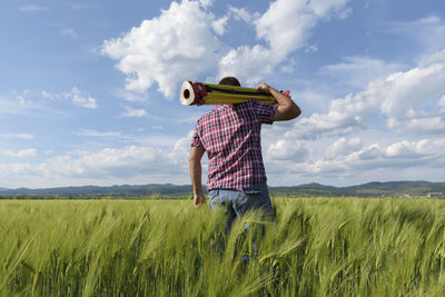 Rear view of engineer with equipment standing on wheat field