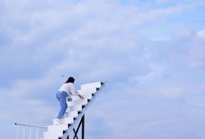 Low angle view of woman climbing on staircase against sky