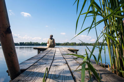 Rear view of man sitting on pier over sea against sky