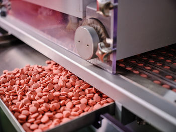 Contemporary pharmaceutical machine with piles of pink pills on conveyor placed in manufacturing laboratory