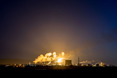 Illuminated factory against sky at night