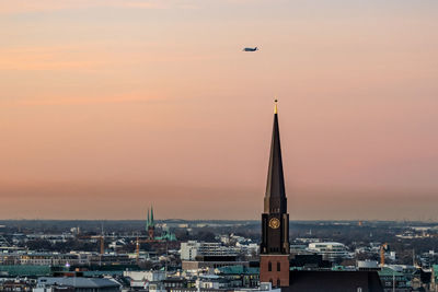 Tower amidst buildings in city against sky during sunset