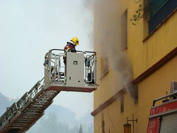 Low angle view of firefighter on cherry picker by smoke coming out from building