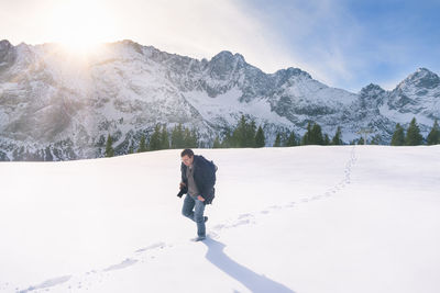 Man walking on snow covered field by mountain