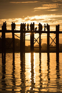 Silhouette people on footbridge over sea against sky during sunset