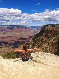 Rear view of woman sitting on mountain against sky