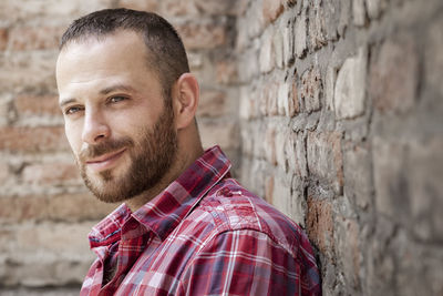 Man looking away while standing against brick wall