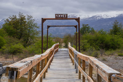 Footbridge amidst trees in forest against sky