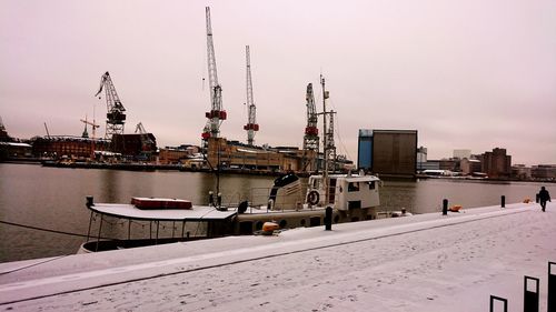 Cranes at harbor against sky during winter