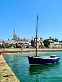 Sailboats moored in canal by buildings against blue sky