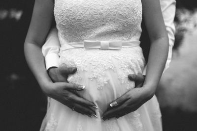 Midsection of groom holding pregnant bride