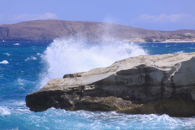 Sea waves splashing on rocks against sky