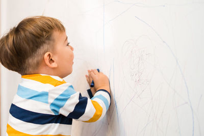 Cute boy drawing on wall at home