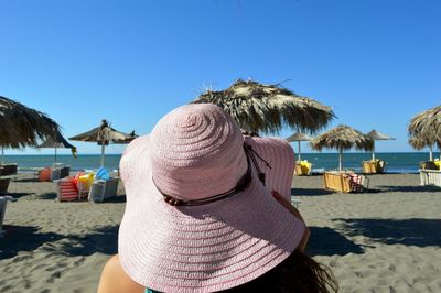 Rear view of woman relaxing on beach against clear blue sky