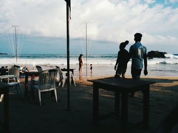 Rear view of friends walking by cafe at sandy beach